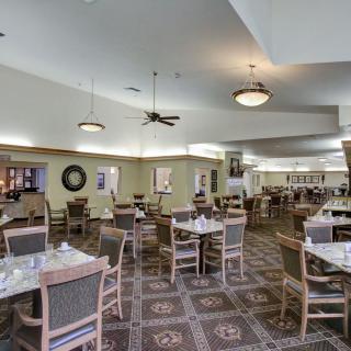 An empty dining area with neatly arranged tables and chairs, featuring ceiling lights and a patterned carpet floor.