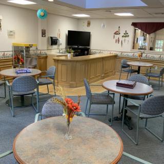 A cozy dining area with several round tables and chairs, a television, and decorative elements including a flower vase on one of the tables.