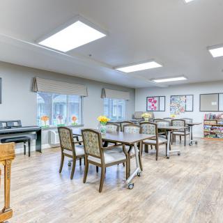 A well-lit dining area with tables and chairs, decorated with artwork on the walls and large windows providing ample natural light.