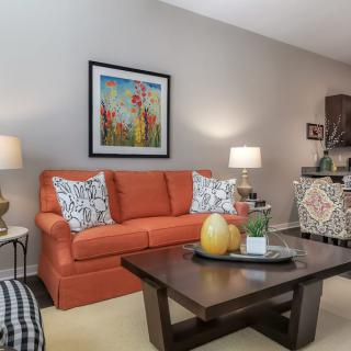 A cozy living room with an orange sofa, colorful artwork, and a wooden coffee table adorned with decorative items.