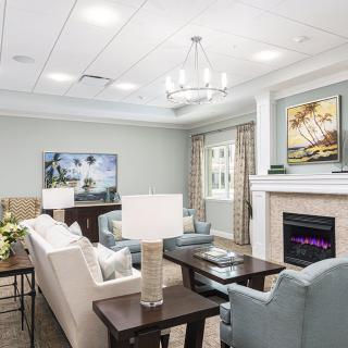 A modern living room with elegant decor, featuring a sofa, chairs, a fireplace, and a chandelier.