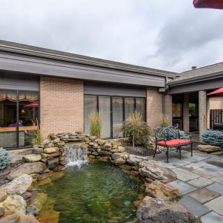 A serene courtyard featuring a pond with a small waterfall, surrounded by stone paths and outdoor seating.