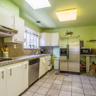 A brightly lit kitchen with green walls, featuring white cabinets and a stainless steel refrigerator.