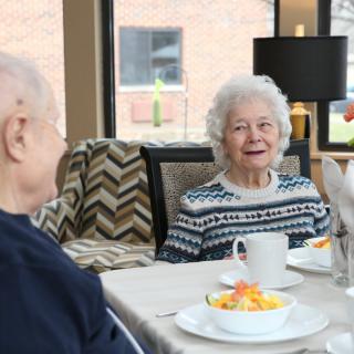 Two elderly people enjoying a meal together at a dining table indoors.