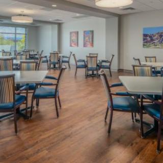 A modern dining area with empty tables and chairs, featuring wooden floors and artwork on the walls.