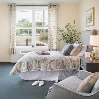 A cozy bedroom with a neatly made bed, elegant decor, and ample natural light streaming through large windows.