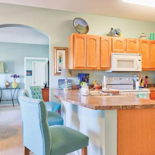 Bright kitchen interior with wooden cabinets and teal bar stools.