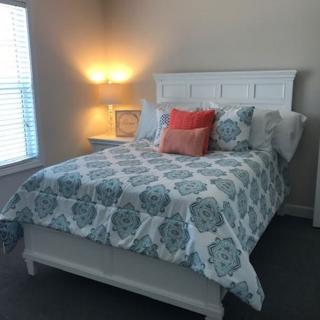 A cozy bedroom with a neatly made bed featuring patterned bedding and accent pillows, lit by a warm bedside lamp.