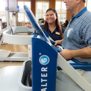 A fitness trainer assists a client on specialized exercise equipment in a rehabilitation setting.
