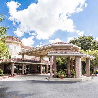 The image shows the entrance of a hotel building with a covered driveway and a clear blue sky overhead.
