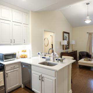 A modern apartment kitchen with white cabinets and a view into the living room.