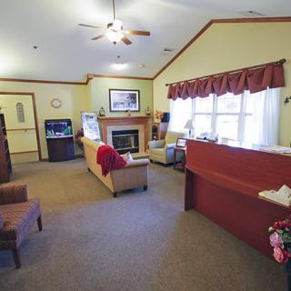 A cozy living room with a sofa, fireplace, and large window, featuring a ceiling fan and carpeted floor.