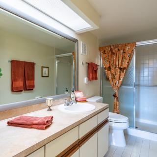 A well-lit bathroom with a large mirror, sink, and shower area.