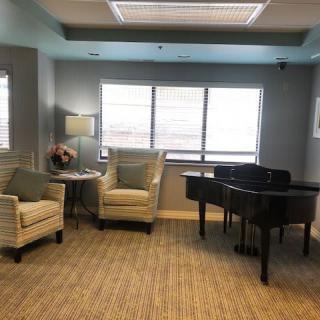 A cozy living room with a piano, two armchairs, a small table, and a lamp by the window.