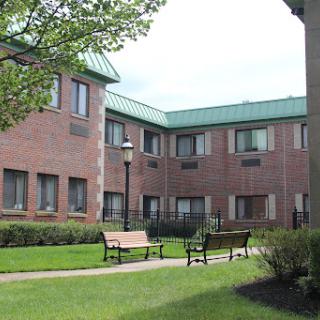 A view of a brick building on a college campus, featuring green roofs and benches in the surrounding lawn.