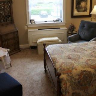 A cozy bedroom with a bed, armchair, and window view.