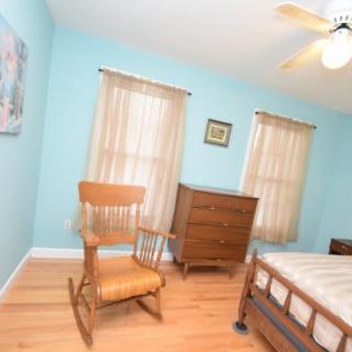 A cozy bedroom with light blue walls, featuring a rocking chair and a wooden dresser.