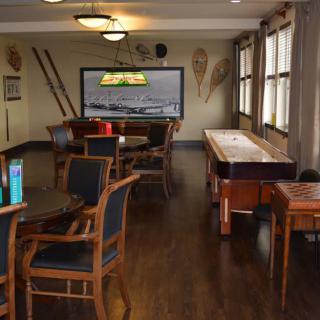 A cozy game room with a shuffleboard table, comfortable seating, and a large television.