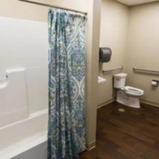 An accessible bathroom featuring a toilet, bathtub with shower curtain, and handrails.