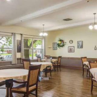 A cozy dining area with several tables and chairs, adorned with wall decorations and large windows letting in natural light.