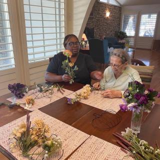 Two people arranging flowers on a table indoors.