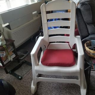 A white plastic chair with a red cushion, set in a cozy indoor environment.