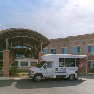 A shuttle bus parked outside a hospital entrance on a sunny day.