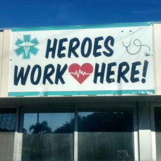 A banner with the message 'Heroes Work Here!' featuring healthcare symbols on a building.
