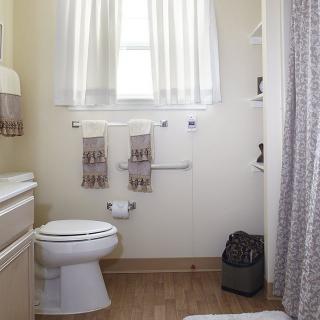 A small, well-lit bathroom with a toilet, neatly hung towels, and a shower curtain.