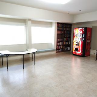 A spacious break room featuring a vending machine and a simple table under large windows.
