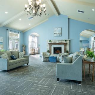 A spacious and elegantly designed living room featuring blue walls, plush sofas, a central fireplace, and a chandelier under a vaulted ceiling.