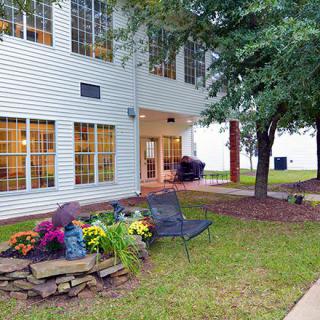A view of a building exterior with a landscaped garden area featuring chairs and vibrant plants.