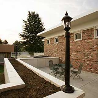 A cozy patio area with outdoor seating, bordered by brick walls and garden beds, featuring a classic black lamp post.