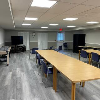 A spacious meeting room with tables, chairs, and a television for presentations.
