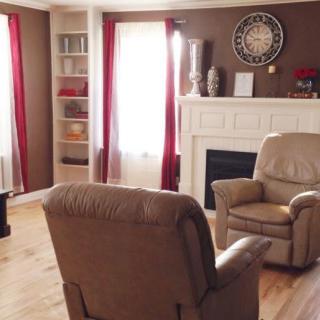 A cozy living room with armchairs, a fireplace, and a large wall clock.