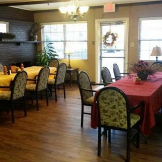 A cozy dining area with tables and chairs set on wood flooring, adorned with decorative plants and warm lighting.