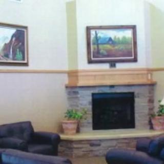 A cozy living room with a fireplace, surrounded by comfortable seating and adorned with paintings and potted plants.