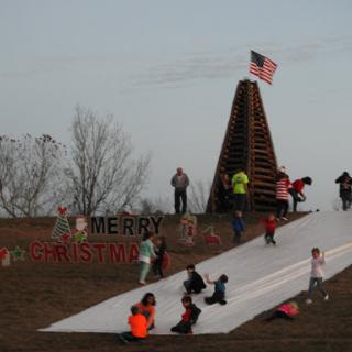 Children enjoying a winter sledding activity near a festive Christmas display.
