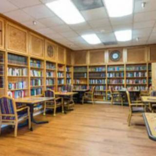 A quiet library room with wooden bookshelves, tables, and chairs for reading and studying.