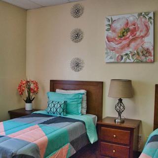A cozy bedroom with twin beds, adorned with colorful bedding and a floral painting on the wall.