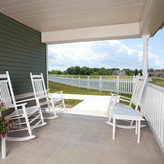 A cozy porch with white rocking chairs overlooking a fenced-in yard.