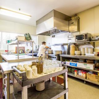 A bustling commercial kitchen with a chef preparing food amidst stainless steel equipment and shelves stocked with various ingredients.