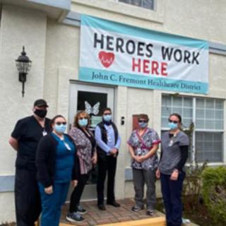 A group of healthcare workers standing outside a building under a banner reading 'Heroes Work Here'.