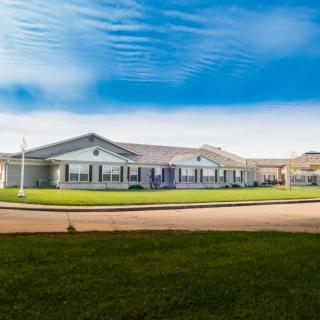 A single-story residential building with a well-maintained lawn under a blue sky with clouds.