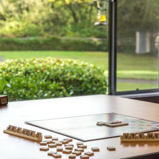 A Scrabble board with tiles scattered on a table by a window overlooking a garden.