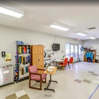 A spacious classroom with chairs, tables, and storage units, featuring a television on the wall.