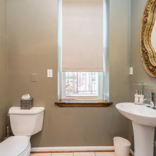 A neatly decorated bathroom with a toilet, sink, and ornate mirror beside a window.