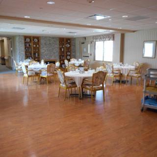 An empty dining room with round tables and chairs arranged neatly on a wooden floor.