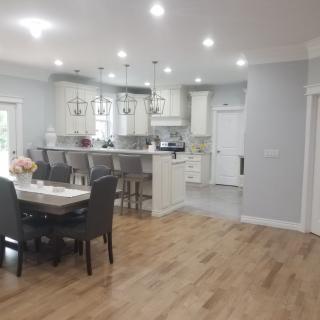 A modern kitchen and dining area with an open layout, featuring hardwood floors, pendant lighting, and a breakfast bar with stools.