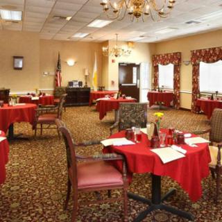 A well-decorated dining area with multiple tables and chairs arranged neatly, featuring chandeliers overhead and an elegant carpet.